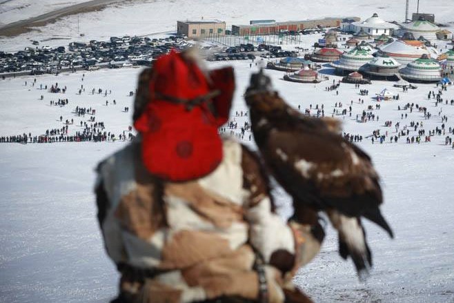 An eagleman is holding his eagle on his hand & watching the audinces at eagle festival in Ulaanbaatar