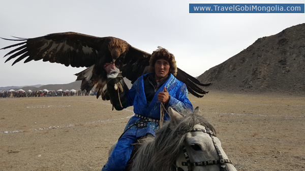a Kazakh man holding his eagle on the hill for competition in eagle festival